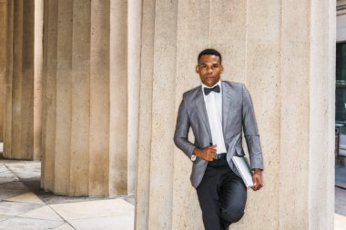 Gri ceketi, papyonu, beyaz atleti, siyah pantolonu, dizüstü bilgisayarı olan genç siyahi bir adam dışarıda durup şöyle düşünüyordu:.