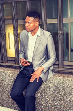 Gri ceketli, beyaz atletli, siyah pantolonlu, New York 'ta eski tarz pencere çerçevesinde oturan, cep telefonu tutan, etrafa bakıp.