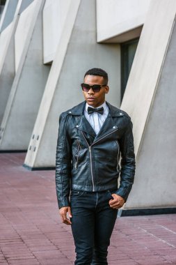 Siyah deri ceket, siyah kot pantolon, güneş gözlüğü, beyaz atlet, siyah papyon, New York 'ta sokakta yürüyen genç bir Afrikalı Amerikalı. Şehir çocuğu.