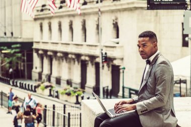 Gri ceketli, papyonlu, sokakta oturan, etrafa bakınan, okuyan, dizüstü bilgisayarında çalışan genç bir zenci. Instagram etkisi.