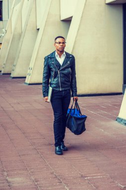 Siyah deri ceket, kot pantolon, deri ayakkabı, gözlük, dizüstü bilgisayar, spor çantası taşıyan, New York 'ta sokakta yürüyen Afrikalı Amerikalı bir üniversite öğrencisi.