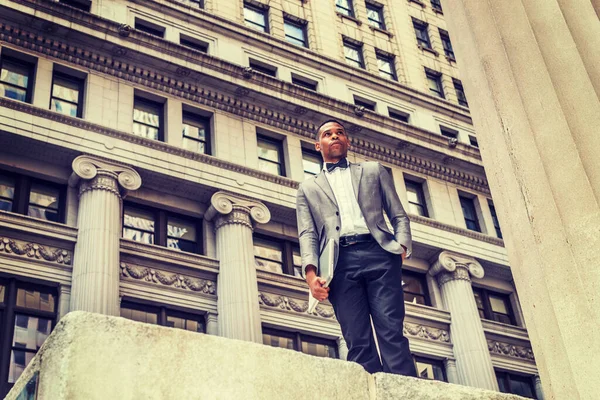 Gri ceketli, papyonlu, siyah pantolonlu, dizüstü bilgisayarlı, sokakta duran genç bir zenci. Kendine güvenerek yukarı bakıyor. Instagram etkisi