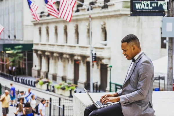 Gri ceketli, papyonlu, Wall Street 'te oturan, gülümseyen, okuyan, dizüstü bilgisayarda çalışan siyah bir adam. Instagram etkisi