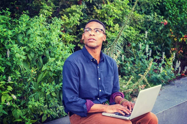 Gözlük takan, kampüste yeşil bitkilerin yanında oturan, dizüstü bilgisayarda çalışan, yukarı bakan, düşünen, umut eden, hayal gücü olan genç bir adam.. 