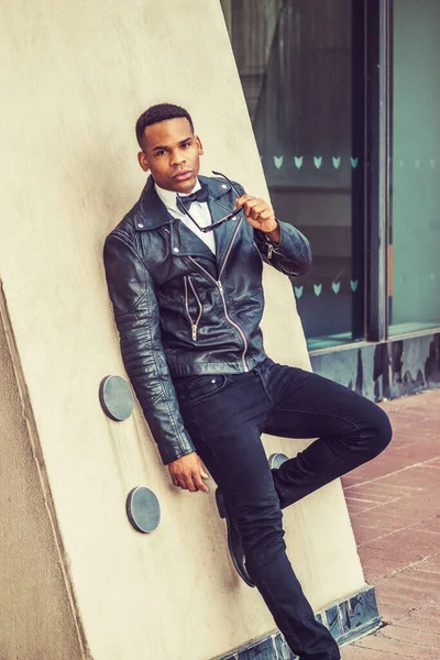 Siyah deri ceket, kot pantolon, beyaz atlet, papyon, güneş gözlüğü, New York sokaklarında duvara yaslanmış genç bir Afrikalı Amerikalı..