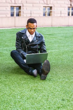 Afrikalı Amerikalı üniversite öğrencisi New York 'ta okuyor. Deri ceketli, kot pantolonlu, deri ayakkabılı, gözlüklü, kampüste yeşil çimlerde oturan, okuyan, dizüstü bilgisayarda çalışan genç bir zenci..