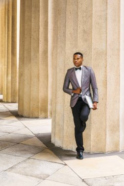 New York 'ta çalışan kendinden emin bir Afrikalı Amerikalı iş adamı. Gri ceketli, papyonlu, siyah pantolonlu, deri ayakkabılı, dizüstü bilgisayarlı, genç siyahi bir adam dışarıda bekliyor..