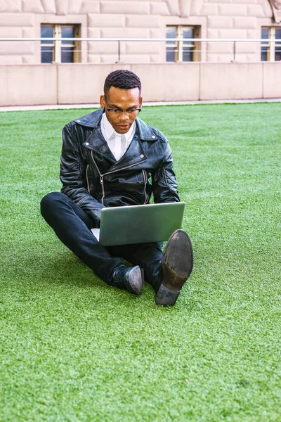 Afrikalı Amerikalı üniversite öğrencisi New York 'ta okuyor. Deri ceketli, kot pantolonlu, deri ayakkabılı, gözlüklü, kampüste yeşil çimlerde oturan, okuyan, dizüstü bilgisayarda çalışan genç bir zenci..