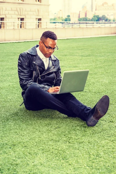 Afrikalı Amerikalı üniversite öğrencisi New York 'ta okuyor. Deri ceketli, kot pantolonlu, deri ayakkabılı, gözlüklü, kampüste yeşil çimlerde oturan, okuyan, dizüstü bilgisayarda çalışan genç bir zenci..