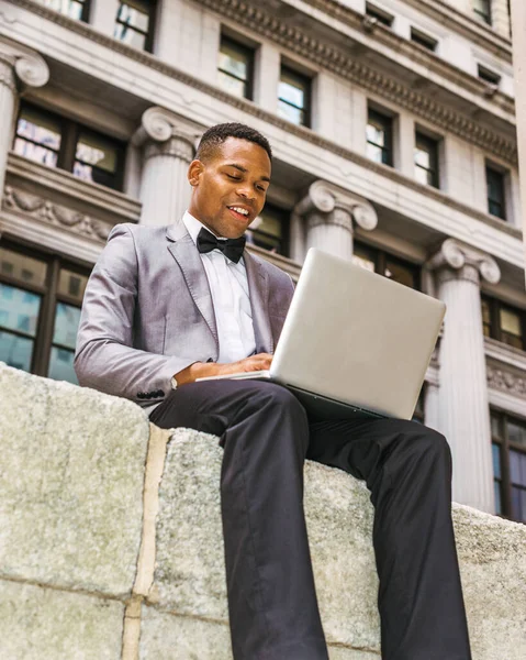 New York 'ta sokakta çalışan Afrikalı Amerikalı iş adamı. Gri ceketli, papyonlu, iş bölgesinde oturan, okuyan, dizüstü bilgisayarda çalışan genç bir zenci. Filtrelenmiş etki.