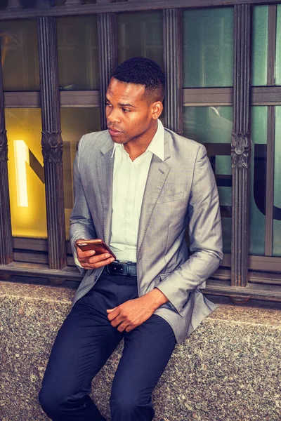 Herhangi bir yere mesaj atıyorum. Gri ceketli, beyaz tişörtlü, siyah pantolonlu, New York 'ta eski tarz pencere çerçevesinde oturan, elinde cep telefonu olan Afro-Amerikan bir adam. Filtrelenmiş etki.