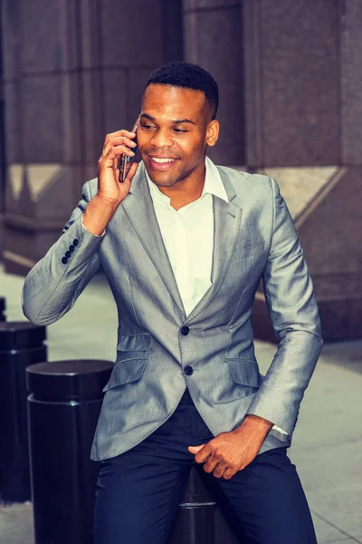 New York 'ta çalışan mutlu Afrika kökenli Amerikalı iş adamı. Gri ceketli, beyaz atletli, siyah pantolonlu, ofisin dışında sokakta oturan, gülümseyen, telefonla konuşan genç bir zenci. Şehir Günlük Yaşamı.