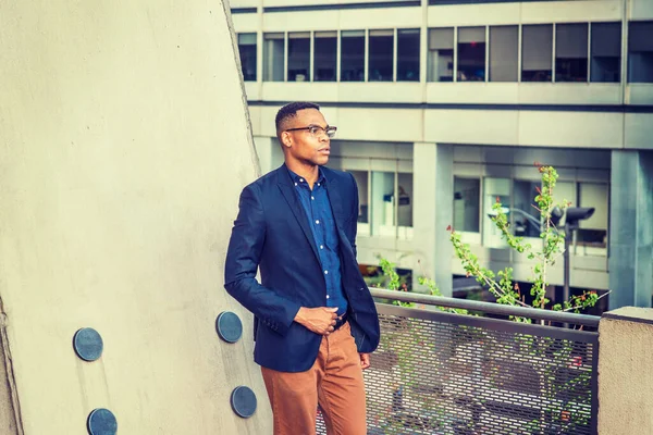 New York 'ta çalışan Afro-Amerikalı iş adamı, mavi ceketli, kahverengi pantolonlu, gözlüklü, balkonda korkuluk başında duran, caddeye bakan, üzgün, düşünen, düşüncelere dalmış. Filtrelenmiş etki.