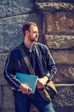 Siyah deri ceket, kot pantolon, omuz çantası, dizüstü bilgisayar sakallı Amerikalı bir adam kayalık duvarın yanında çalışmaya hazır bekliyor. Filtrelenmiş etki