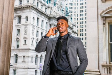 New York 'ta çalışan Afrikalı Amerikalı iş adamı. Modaya uygun bir ceket, siyah atlet, kravat, küçük keçi sakallı genç adam, klasik tarz ofis binasının yanında duruyor, cep telefonundan arıyor.