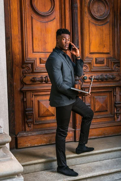 New York 'ta çalışan Afrikalı Amerikalı iş adamı. Modaya uygun ceketi, siyah kravatı, pantolonu, ayakkabıları, klasik tarz kapı aralığında duran, dizüstü bilgisayarla çalışan, telefonla arayan genç bir adam.