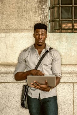 New York 'ta okuyan, gri tişörtlü, omuz çantalı, sokakta duvara yaslanmış, kitap okuyan, dizüstü bilgisayarla çalışan Afrikalı Amerikalı bir üniversite öğrencisi. Renkli filtrelenmiş efekt