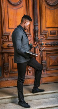 New York 'ta çalışan meşgul bir Afrikalı Amerikalı iş adamı, şık bir ceket giyiyor, klasik kütüphane kapısından merdivenlere çıkıyor, aşağıya bakıyor, dizüstü bilgisayarında çalışıyor, telefondaki mesajları okuyor.