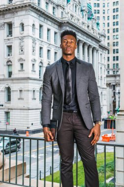 New York 'ta keçi sakallı Afrikalı iş adamı, şık bir ceket, siyah atlet, kravat, kol saati, tablet bilgisayar, klasik ofis binalarının yanında duruyor.