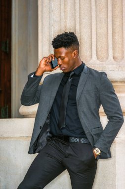 New York 'ta çalışan Afro-Amerikalı iş adamı, şık bir ceket, kravat, kol saati takıyor, köşenin dışında duruyor, aşağıya bakıyor, cep telefonunu dinliyor. filtrelenmiş etki.