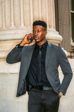 New York 'ta çalışan Afro-Amerikalı iş adamı, şık bir ceket giyiyor, siyah kravat takıyor, kol saati takıyor, ofisin dışında cep telefonu dinliyor. filtrelenmiş etki