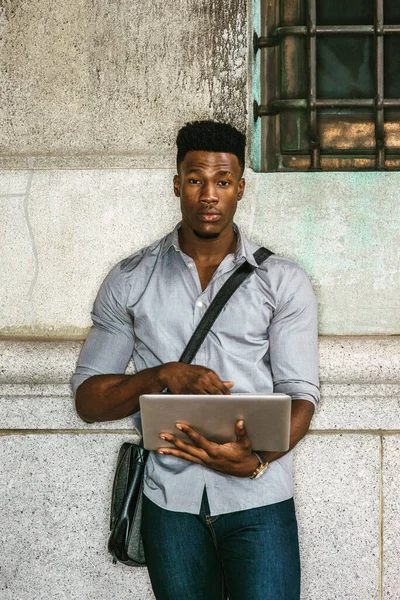 New York 'ta okuyan Afro-Amerikan Kolej öğrencisi, gömlek giyiyor, deri çanta taşıyor, sokakta duvara yaslanıyor, okuyor, dizüstü bilgisayarla çalışıyor. filtrelenmiş etki