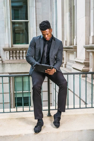 Modern okuma. New York 'ta çalışan Afro-Amerikalı iş adamı, şık bir ceket giyiyor, siyah kravat takıyor, ofis binasında parmaklıklara oturuyor, elinde tablet bilgisayar tutuyor, okuyor, düşünüyor, planlıyor.