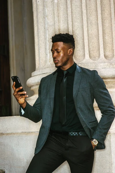 New York 'ta çalışan Afro-Amerikalı iş adamı, şık bir ceket giymiş, siyah kravat takmış, klasik ofis kapısında duruyor, cep telefonundan mesajlar okuyor, düşünüyor. filtrelenmiş etki