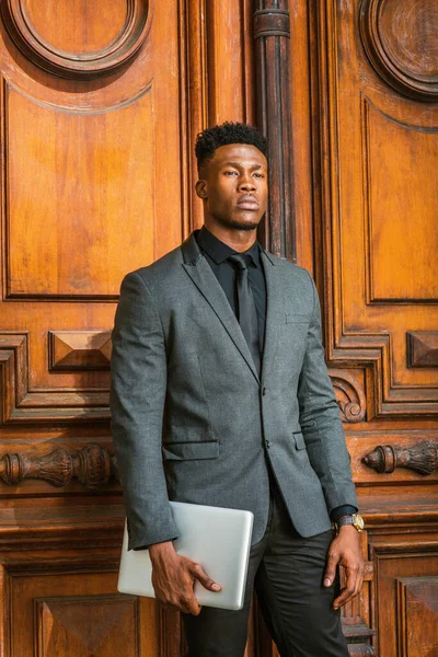New York 'ta küçük keçi sakallı Afrikalı iş adamı, şık bir ceket, siyah atlet, kravat, kol saati, dizüstü bilgisayar, klasik tarz kapı aralığının yanında duruyor.