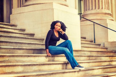 Siyah uzun kollu, V yakalı, kot pantolonlu, deri ayakkabılı, New York 'ta ofis binasında merdivenlerde oturan Afro-Amerikan bir üniversite öğrencisi..