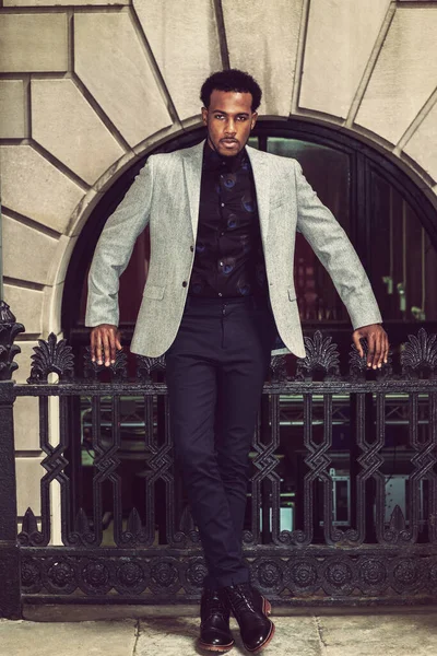 New York 'ta çalışan Afro-Amerikalı iş adamı, gri ceketli, çiçekli atlet, pantolon, deri çizmeli, korkulukların yanında duran, gergin bir şekilde sana bakan.. 