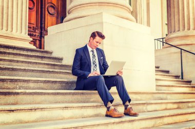 Amerikalı iş adamı seyahat ediyor, New York 'ta çalışıyor, siyah takım elbise, kravat, beyaz atlet, sarı deri ayakkabı giyiyor, klasik ofisin önünde oturuyor, dizüstü bilgisayarla çalışıyor.