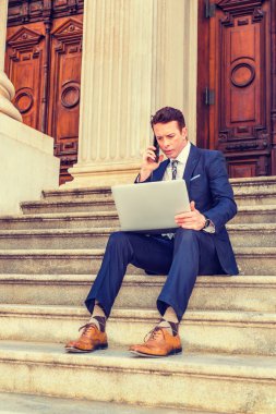 Amerikalı iş adamı seyahat ediyor, New York 'ta çalışıyor, siyah takım elbise, kravat, sarı deri ayakkabı giyiyor, klasik ofisin merdivenlerinde oturuyor, dizüstü bilgisayarla çalışıyor, telefonla arıyor.