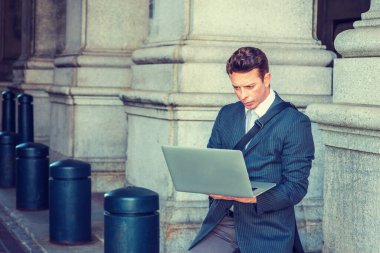 Amerikalı iş adamı seyahat ediyor, New York 'ta çalışıyor, çizgili ceket giyiyor, omuz çantası taşıyor, sokak sütununda oturuyor, aşağı bakıyor, okuyor, dizüstü bilgisayarla çalışıyor.. 