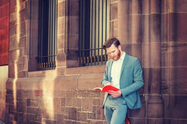 New York 'ta sakallı, bıyıklı, mavi takım elbiseli, beyaz tişörtlü, kampüste pencereleri olan, kırmızı kitap okuyan Amerikalı mezun öğrenci..