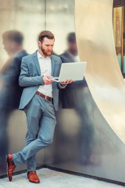 New York 'ta çalışan sakallı, bıyıklı, asker üniformalı, beyaz gömlekli, kahverengi deri ayakkabılı, metal duvarda duran, dizüstü bilgisayarla çalışan Amerikalı bir iş adamı.. 