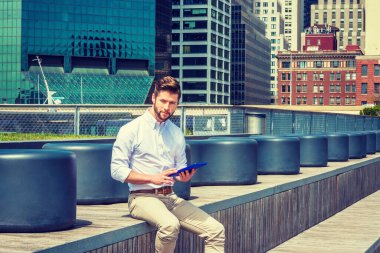 Modern okuma. Sakallı, beyaz tişörtlü, esmer pantolonlu Amerikalı bir adam. New York 'ta iş alanında merdivenlerde oturmuş tablet bilgisayar okuyor.. 