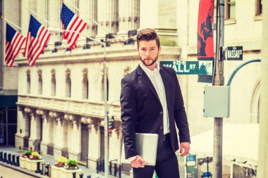 New York 'ta çalışan sakallı bir iş adamı, siyah takım elbiseli, beyaz tişörtlü, dizüstü bilgisayarlı, Wall Street' in dışında Amerikan bayraklarıyla duruyor.. 