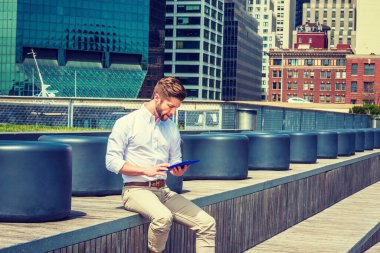 Modern okuma. Sakallı, beyaz tişörtlü, esmer pantolonlu Amerikalı bir adam. New York 'ta iş alanında merdivenlerde oturmuş tablet bilgisayar okuyor.. 