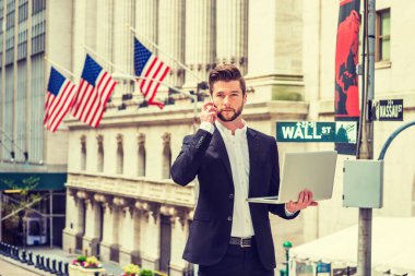 Modern gündelik hayatımızda teknolojinin gücü. Siyah takım elbiseli, New York 'ta Wall Street' te sakallı Amerikalı iş adamı dizüstü bilgisayarla çalışıyor, cep telefonuyla konuşuyor..