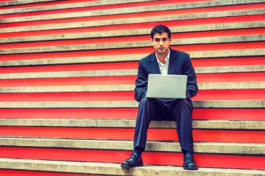 Başarının yolu. Doğu Hindistan Amerikan Koleji öğrencisi, New York 'ta okuyor, siyah takım elbise, beyaz gömlek, deri ayakkabı giyiyor, merdivenlerde oturuyor, dizüstü bilgisayarla çalışıyor..