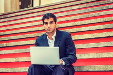 Başarının yolu. Doğu Hindistan Amerikan Koleji öğrencisi, New York 'ta okuyor, siyah takım elbiseli, beyaz gömlekli, kampüste merdivenlerde oturuyor, dizüstü bilgisayarla çalışıyor.. 