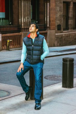 Doğu Hindistan Amerikan Koleji öğrencisi uzun kollu tişört giyiyor, mavi yelek, kot pantolon, deri ayakkabı giyiyor, New York 'ta eski bir caddede oturuyor,. 