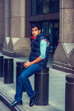 Modern Şehir Hayatı. Doğu Hindistan Amerikan Koleji öğrencisi uzun kollu tişört giyiyor, mavi yelek, kot pantolon, deri ayakkabı giyiyor, New York 'ta sokak sütununda oturuyor, mesajlaşıyor.. 