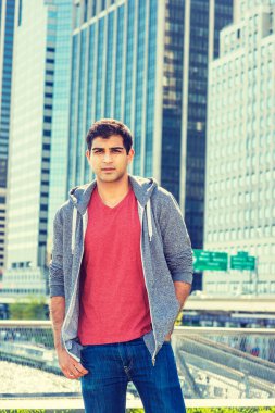Şehir çocuğunun portresi. Doğu Hintli Amerikalı üniversite öğrencisi New York 'ta seyahat ediyor, kırmızı v yaka tişörtü, gri kapüşonlu sweatshirt, iş yerinin önünde duruyor.. 