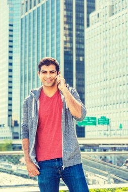 New York 'ta seyahat eden, gri kapüşonlu sweatshirt giyen, iş yerinin önünde duran, cep telefonuyla konuşan, gülümseyen mutlu Doğu Hintli Amerikalı üniversite öğrencisi.. 