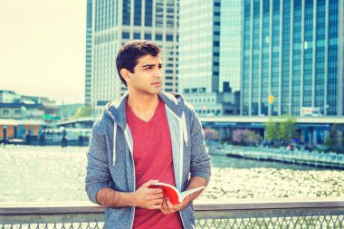 Doğu Hint asıllı Amerikalı üniversite öğrencisi, New York 'ta okuyor, kırmızı v yaka tişörtü giyiyor, gri kapüşonlu sweatshirt giyiyor, iş bölgesinde duruyor, kırmızı kitap okuyor,. 