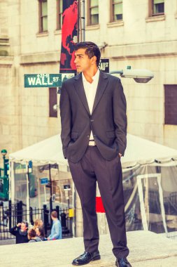 Siyah takım elbiseli, beyaz gömlekli, elleri ceplerinde, genç Doğu Hintli Amerikalı adam New York 'ta Wall Street tabelasıyla sokakta duruyor, etrafa bakıyor.. 