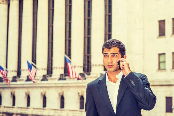 East Indian American Business Man travels, works in New York. Wearing black suit, white shirt, college student stands on street outside office, listens, talks on cell phone.