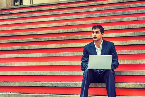 Way to Success. East Indian American College Student studies in New York. Wearing black suit, white shirt, young man sits on stairs on campus, works on laptop computer, thinks.